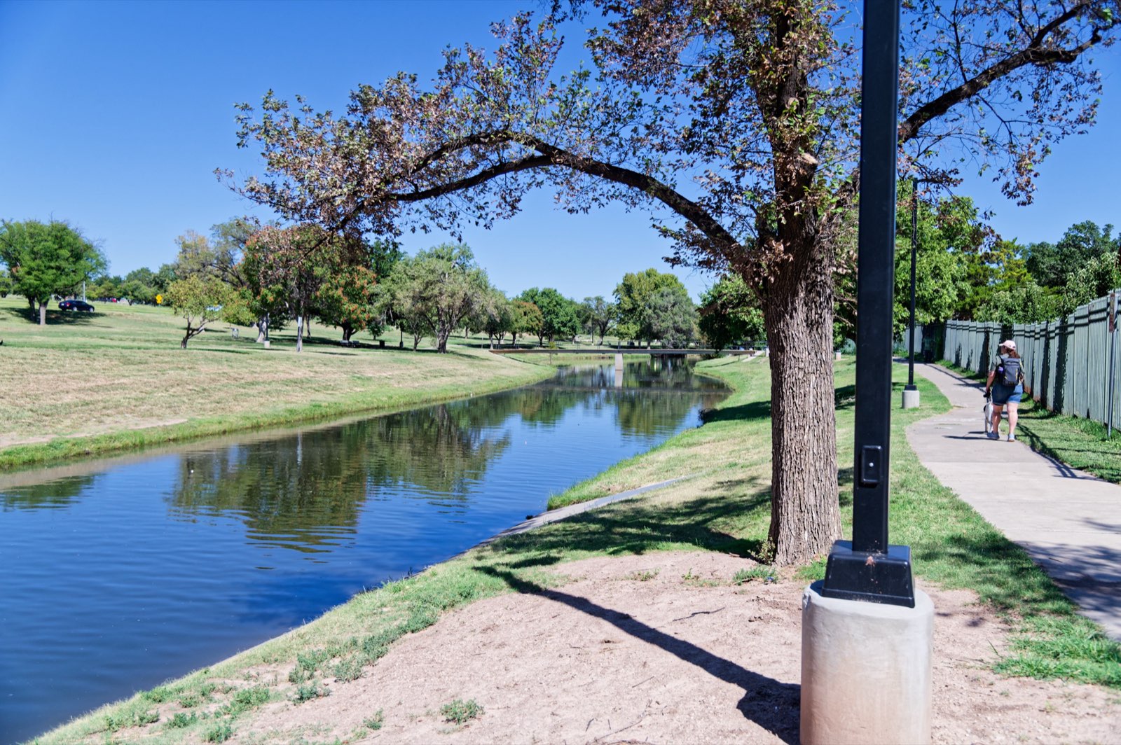 A path running beside a canal lined with trees under a blue sky.